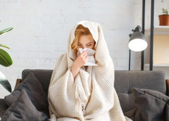 Woman wrapped in blanket drinking hot beverage indoors, illustrating how air conditioning systems can create uneven cooling and comfort issues in modern homes